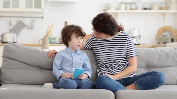 Máma s dětmi na pohovce vychutnat video na mobilním telefonu šeptá v uchu tráví čas doma spolu