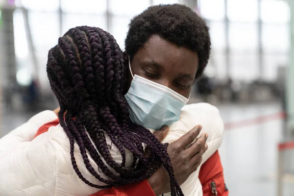 Black couple met in airport after separation due to covid. Romantic man in mask give woman warm hug