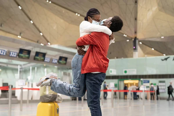 African couple reunion under covid-19 new normality. Cheerful man and woman in masks hug in airport — Stock Photo, Image