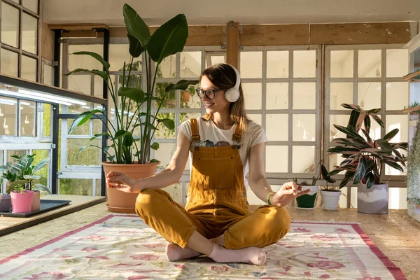 Genç bahçıvan kadın meditasyon yapıyor. Tulum giymiş güzel bir kadın ve kulaklık. Çalışmaktan ya da işten uzak durur. — Stok fotoğraf