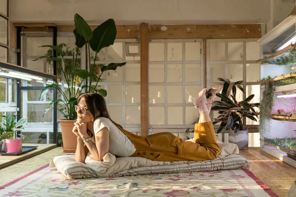 Girl gardener lying on floor in greenhouse or home garden room with houseplants and in flower pots — Stock Photo, Image
