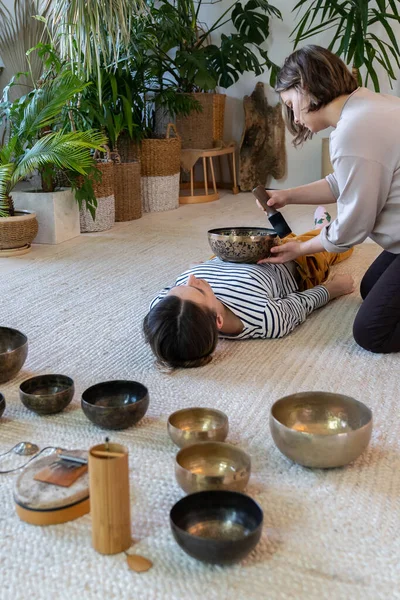 Les jeunes femmes pratiquent la massothérapie sonore avec des bols chantants tibétains. Concept de médecine alternative — Photo