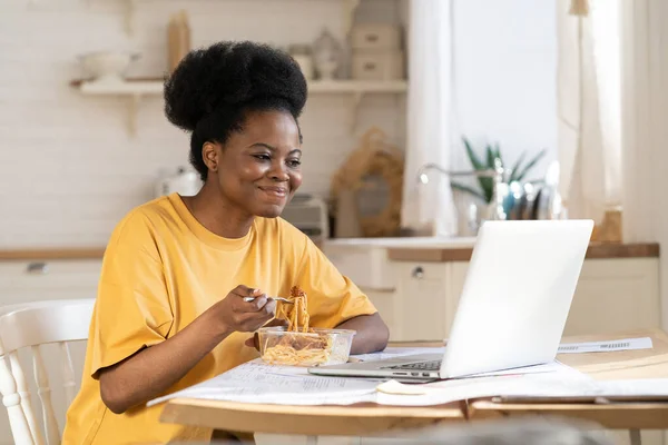 Mujer africana comer y ver vídeo o webinar en el ordenador portátil o hacer una llamada de conferencia a amigos en el descanso —  Fotos de Stock