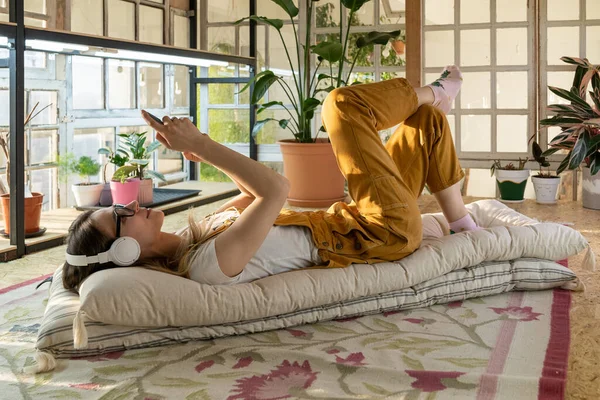 Florista chica descansando en el jardín del hogar después del trabajo, mensajería en el teléfono inteligente escuchar música clásica — Foto de Stock