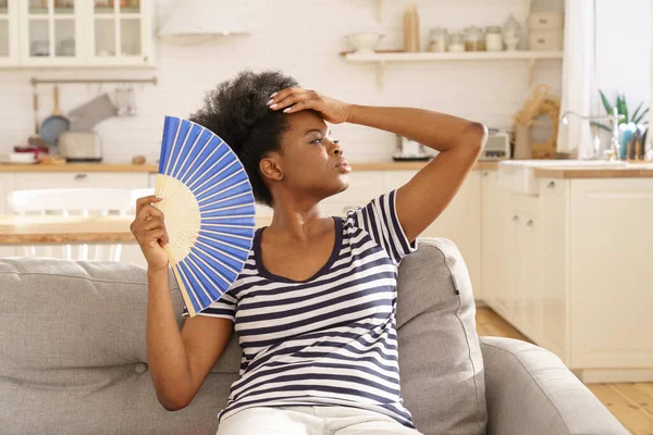 Millennial zwarte vrouw last van hitteberoerte, hete temperatuur thuis gebruik papier ventilator voor frisse lucht — Stockfoto