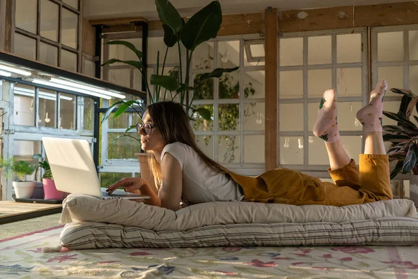 Flicka använda laptop ligger på golvet i rummet med retro möbler och växter. Florist slappna av efter jobbet — Stockfoto