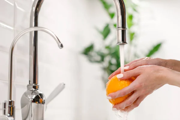 洗面所の台所で蛇口の下に熟したオレンジを洗う女性の手 — ストック写真