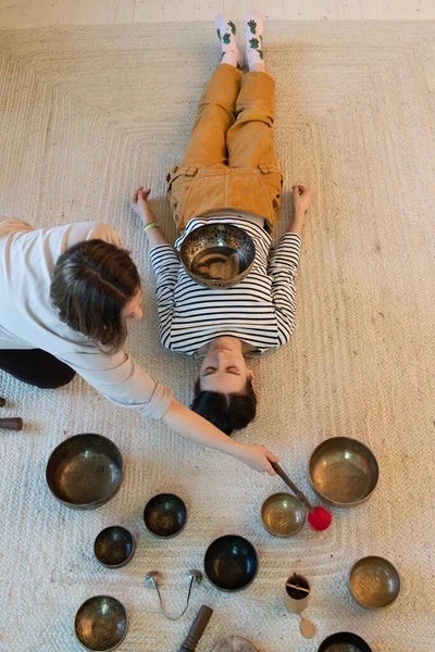 Тибетская терапия с чашами для пения: девушка получает звуковой массаж с бронзовыми блюдами дома для отдыха — стоковое фото