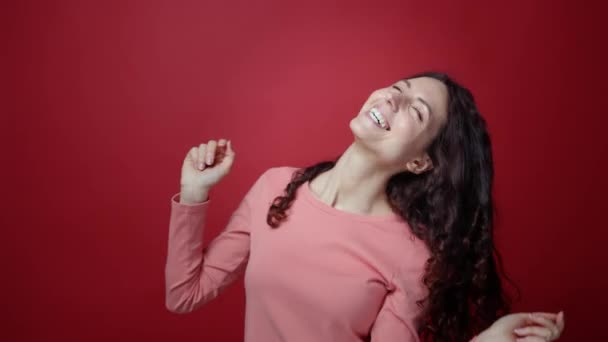 Close-up van vrolijke brunette vrouwelijke happy dance, spelen met mooie krullend haar bij rode studio muur — Stockvideo