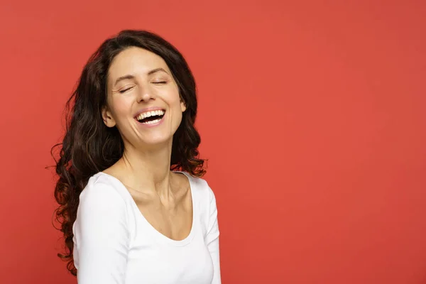 Jonge zorgeloze vrouw met een vrolijke tand glimlach, gesloten ogen, pure huid over koraal studio achtergrond — Stockfoto