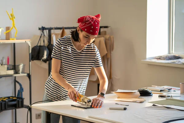 작업실에서 일하는 재단사 야. 전기 칼로 재봉틀을 만드는 여자 옷 디자이너 — 스톡 사진