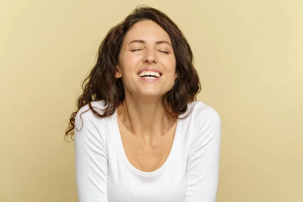 Mujer feliz del milenio con los ojos cerrados sonreír a la cámara sobre la pared beige. Retrato de la risa femenina — Foto de Stock