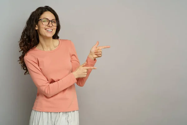 Glückliche Frauen zeigen mit den Fingern auf den Raum über der grauen Wand. Studioporträt einer Geschäftsfrau zeigt Richtung — Stockfoto