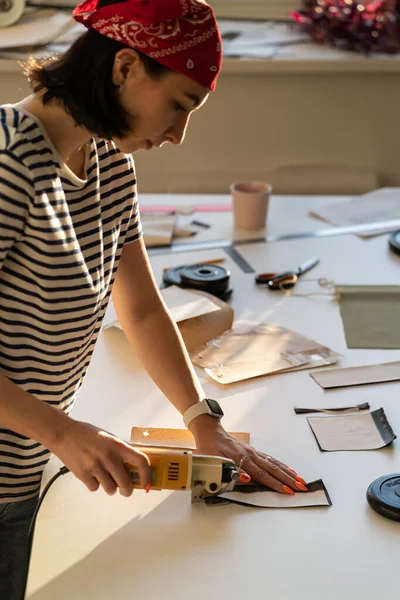 Zajęty krawiec w studio. Kobieta ubrania projektant cięcia tkaniny do szycia z przecinakiem elektrycznym — Zdjęcie stockowe