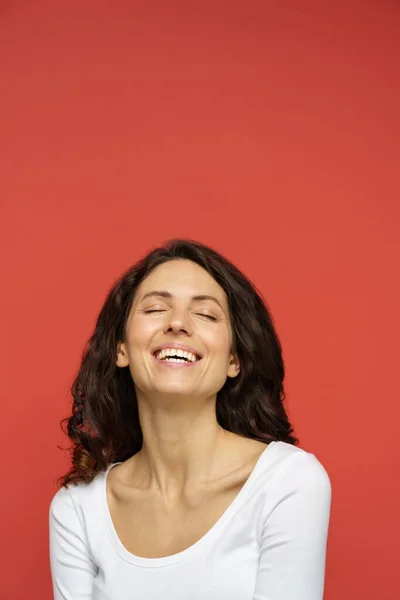 Portret van zorgeloze vrouw in de 30 met gesloten ogen, perfecte huid, witte glimlach op rode achtergrond — Stockfoto