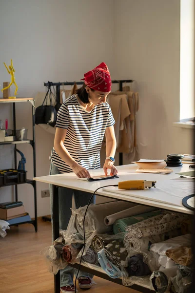 Занятой портной на работе в студии. Женская одежда дизайнер вырезать ткань для шитья с электрическим резаком — стоковое фото