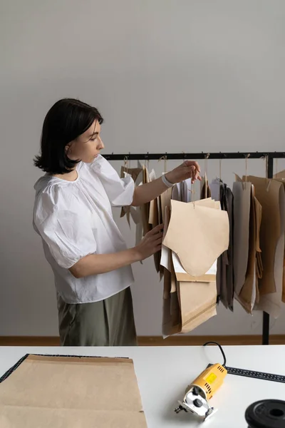 Dressmaking process: fashion designer in trendy clothes hold hangers with paper patterns in studio — Stock Photo, Image