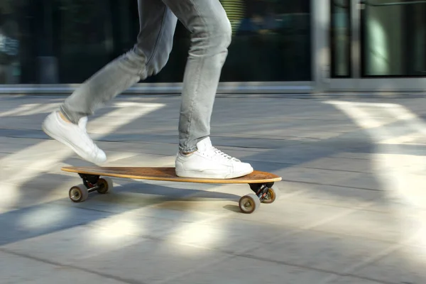 Male skateboarder riding and practicing longboard in the city, outdoors, in motion, cropped image. Man down the street with skateboard. Leisure, healthy lifestyle, extreme sports