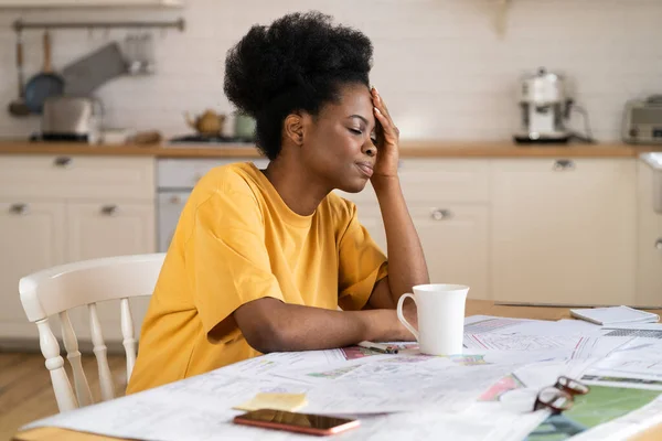 Frustrated black business woman worried with problem sit in kitchen work from home suffer headache