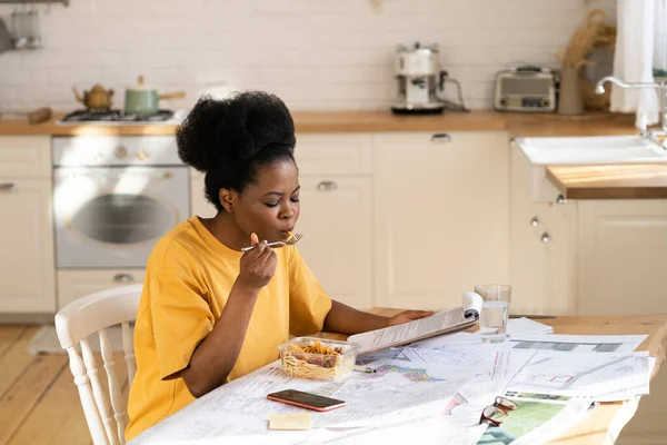 Umtriebige afrikanische Arbeiter oder Studenten essen Mittagessen aus dem Imbisscontainer, lesen Dokumente nach Feierabend zu Hause — Stockfoto