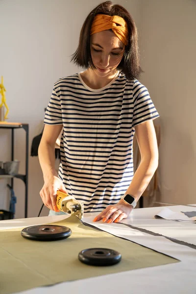 Corte y costura en estudio de sastre: mujer joven de alcantarillado trabaja con tela en estudio de taller de diseño — Foto de Stock