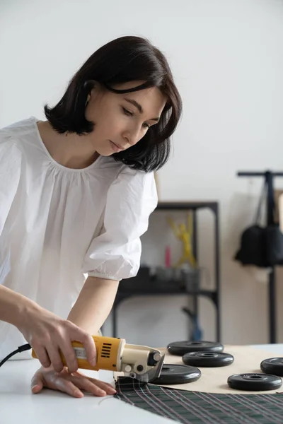 Meisje op maat of jonge mode-ontwerper gebruik elektrische cutter om materiaal voor kleding te snijden in de werkplaats — Stockfoto