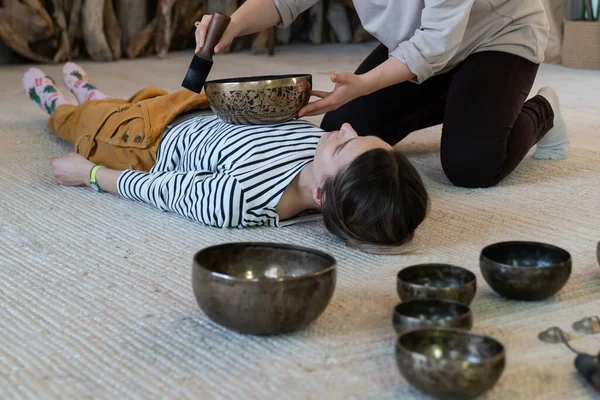 Young woman has tibet massage, singing bowl therapy with traditional tibetan bronze cymbals at home