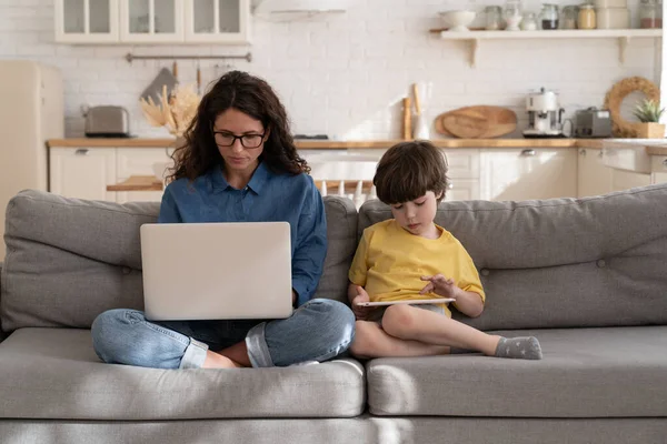 Mère concentrée, fils utilisent ordinateur portable et tablettes assis sur le canapé dans le travail du salon et d'étude — Photo