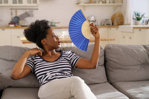 エアコンのない平たい熱中症に苦しむ黒人女性ファンを振ってソファに横たわっ自宅 — ストック写真