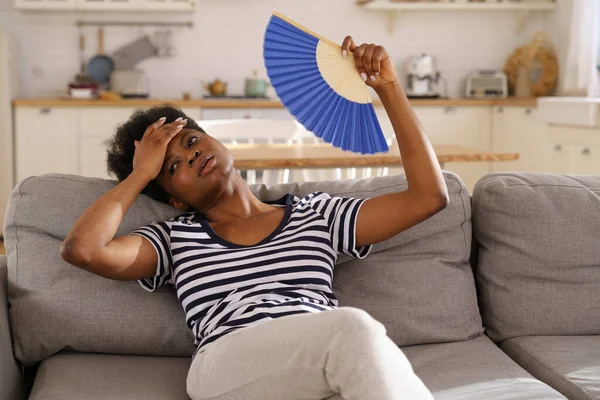 Zwarte vrouw die lijdt aan een hitteberoerte plat zonder airconditioner zwaaien ventilator liggend op de bank thuis — Stockfoto