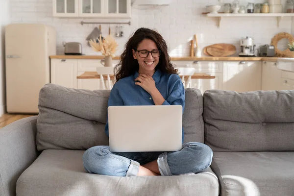 Vrolijke vrouw lachen van video of chat bericht na het werk ontspannen met laptop op de bank in de woonkamer — Stockfoto