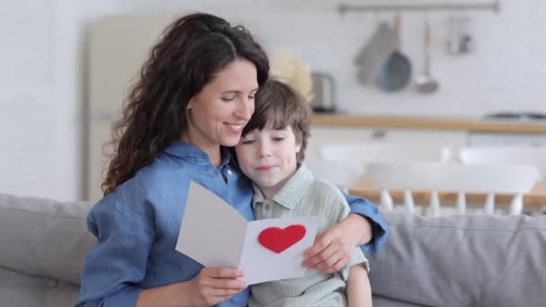 Zorgzame zoon geven mam wenskaart voor vakantie moeder dag of verjaardag zitten knuffelen moeder lees ansichtkaart — Stockvideo