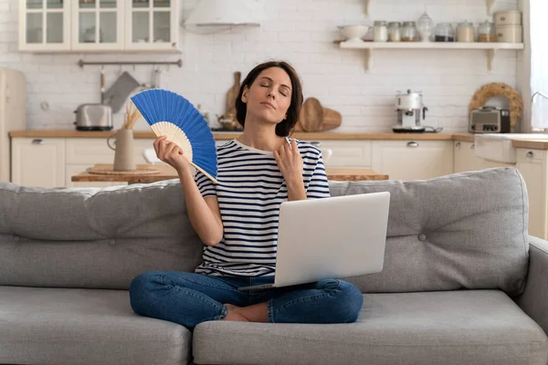 Mladá žena trpí úpal byt bez klimatizace mávání ventilátor sedí na gauči doma — Stock fotografie