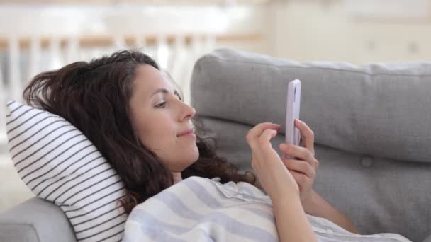 Relaxado jovem deitado no sofá com mensagem de tipo de smartphone ou navegar aplicativos móveis no celular em casa — Vídeo de Stock