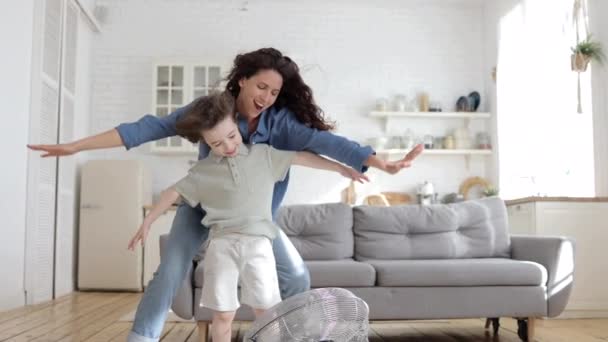 Jovem mãe solteira brincalhão e filho criança pré-escolar se divertir com ventilador indoor soprar vento fresco em casa — Vídeo de Stock