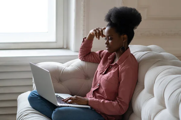 Femme noire assise sur le canapé parlant sur le chat vidéo en ligne ou webinaire à la maison, bavardant, utilisant un ordinateur portable — Photo
