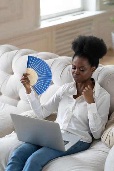 Afro femme d'affaires souffrant de coup de chaleur assis dans le salon à la maison en utilisant ventilateur — Photo