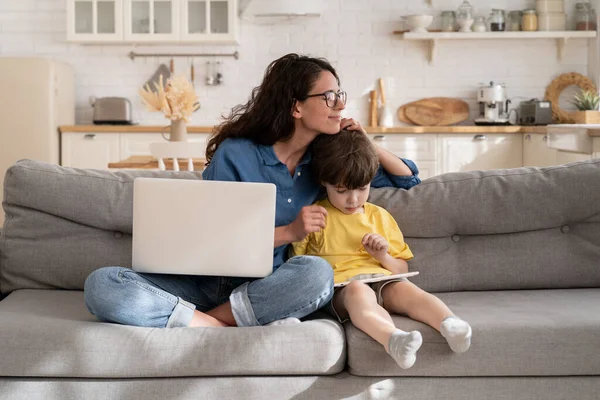 Mère attentionnée femme d'affaires heureux de travailler de la maison sur quarantaine étreinte fils jouer sur tablette numérique — Photo