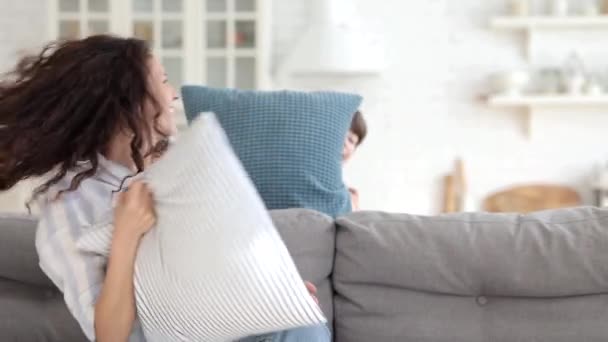Nettes Kind und fröhliche verspielte Mutter kämpfen Kissen auf Couch im Wohnzimmer lachen und entspannen zusammen — Stockvideo