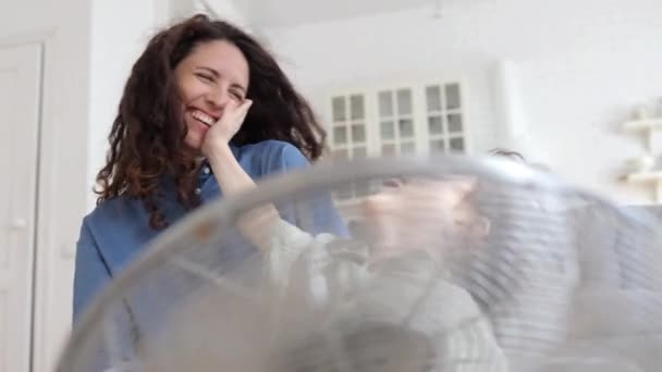 Mamá mantenga pequeño niño delante del ventilador de ventilador de viento soplado en la acogedora sala de estar divertirse con el niño — Vídeos de Stock