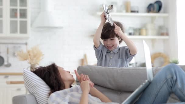 Hyperaktiver Sohn stört müde Mutter auf Sofa im Wohnzimmer liegend mit Laptop-Arbeit oder entspannen Video ansehen — Stockvideo