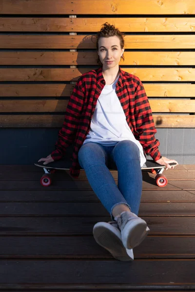 Молода стильна дівчина скейтбордист відпочиває після догбордингу сидить на відкритому повітрі на дошці ковзанки посміхаючись — стокове фото