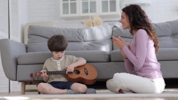 子供がウクレレを学ぶのを見て喜ぶママ。就学前の少年音楽を教える女性教師 — ストック動画