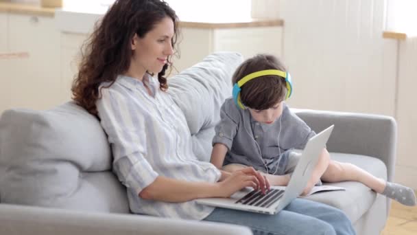Familj lockdown livsstil: son be mamma hjälp med läxor som mamma affärskvinna arbeta på bärbar dator — Stockvideo
