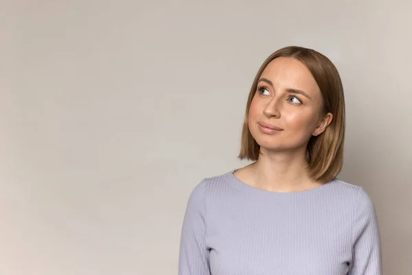 Young casual woman millennial look away to side with curious smile to empty corner over studio wall — Stock Photo, Image