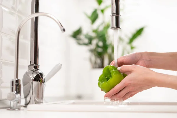 Wash before eat: female washing green pepper in water in sink before cooking salad. Hygiene concept