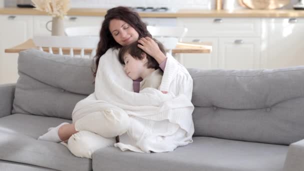 Loving mother embrace cute boy of five sitting on sofa covered with knitted blanket. Love and care — Stock Video