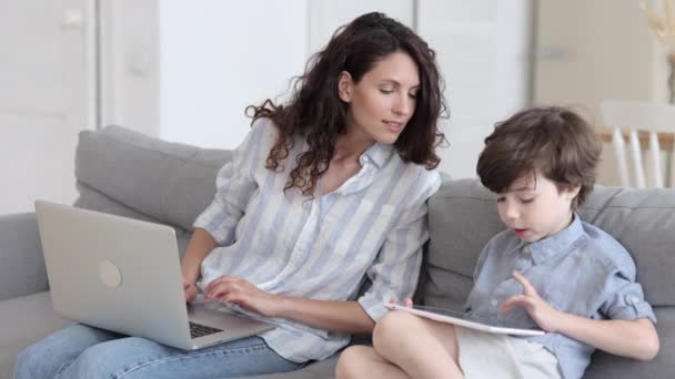 Ensamstående mamma frilansare eller distansarbetare hjälpa förskolan son spela spel eller göra läxor på digital tablett — Stockvideo