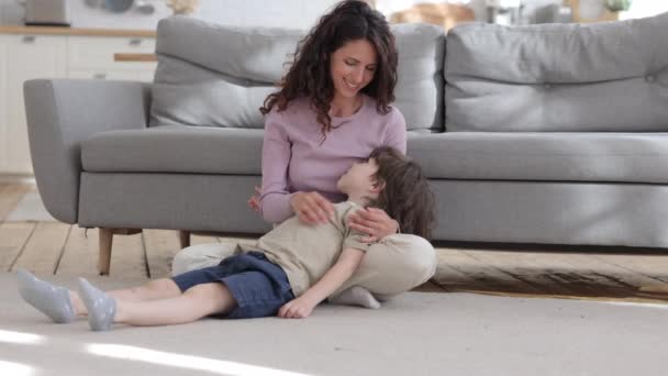 Överlycklig mamma har kul med liten unge kittlande pojke sitter på golvet matta i vardagsrummet skrattar — Stockvideo