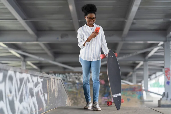 African girl skater with longboard hold phone read networks notification in space for skateboarders
